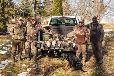 A hunting party of five standing with their black lab behind a truck tailgate full of harvested birds.