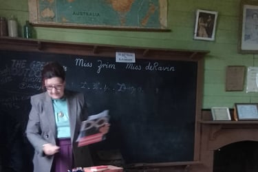 An Old Tailem Town teacher stands before a vintage blackboard in our historic classroom