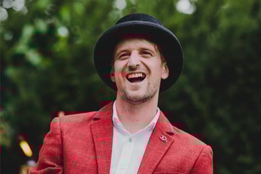 Bräutigam in rotem Anzug und Hut lacht.