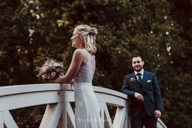 Groom looking at bride on a wooden bridge.
