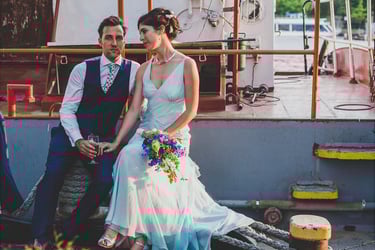 A portrait of the bride and groom sitting next to a boat.