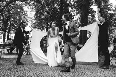 Bride and groom walking through a bed sheet with a heart cut out.