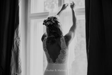 Bride taking down her veil from a hanger in a window.