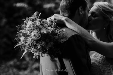 Close-up of bridal bouquet with the newlyweds kissing in the background.