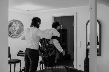 Best man helping groom put on a vest.