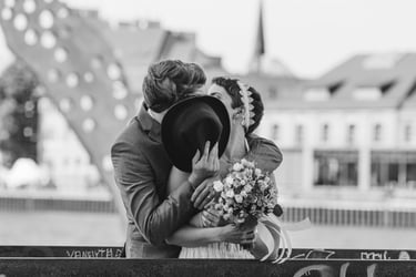 Groom covering his and bride's face with a hat while they kiss.