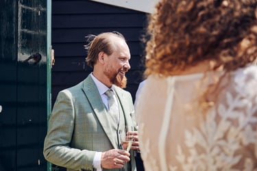 Groom in a green suit talking to wedding guests.
