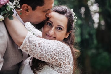 Bride looking into the camera and being kissed on her temple by the groom.