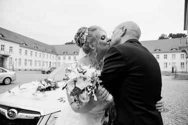 Bride and groom kissing in front of a car.