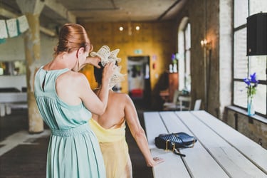 A bridesmaid in a blue dress pinning on a headpiece on the mother of the bride's head.