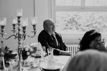 Father of the groom sitting at a table next to a window.