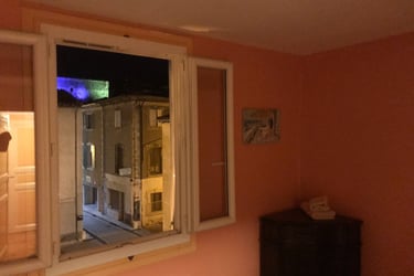 View of a historic Quillan Castle at night through an open window of a peach-colored room.