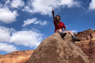 a woman sitting on a rock with her hand up to the sky