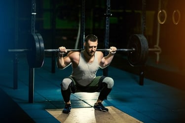 A muscular man performing a heavy barbell back squat in a dark gym for strength training.