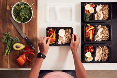 A person preparing healthy meal prep containers with chicken, brown rice, and fresh vegetables.