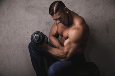 Muscular man performing a heavy dumbbell bicep curl for strength training in a gym setting.