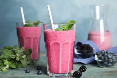 Two glasses of healthy mixed berry smoothies with fresh mint, blueberries, and blackberries.