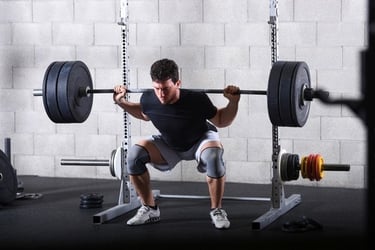 A man performing a heavy barbell back squat in a power rack at a gym.