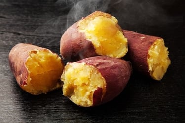 Steaming roasted Japanese sweet potatoes broken open to show soft yellow flesh on a dark surface.