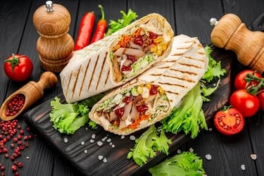 Grilled chicken shawarma wrap cut in half on a wooden board with fresh tomatoes and lettuce.