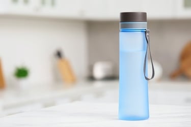 A reusable blue frosted water bottle with a carrying strap on a kitchen counter.