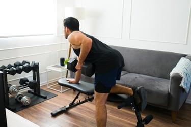 A man performing a dumbbell row exercise on a weight bench in a home gym setting.