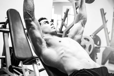 Muscular man performing an incline dumbbell chest press during a bodybuilding gym workout.