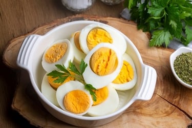 Hard-boiled egg halves served in a white bowl on a wooden board with fresh parsley garnishes.