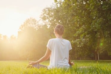 A woman practicing outdoor yoga and meditation in a sunny green park during sunset.