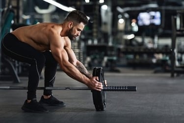 Muscular man loading heavy weight plates onto a barbell for bodybuilding training in a gym.