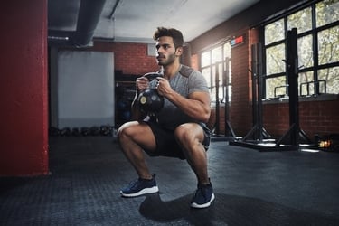 Athletic man performing a goblet squat with a kettlebell during a workout in a gym.