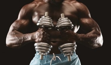 Muscular male bodybuilder lifting silver chrome dumbbells for strength training.