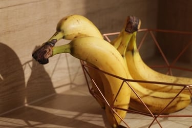 Fresh ripe yellow bananas in a modern copper wire fruit basket on a wooden countertop.