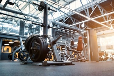 Weight plate rack with heavy barbell plates in a modern industrial gym facility with strength training equipment.