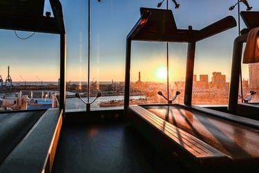 Treadmills in a modern fitness center overlooking a city harbor during a vibrant sunset.