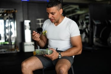 A muscular man in gym clothes eating a healthy salad for post-workout nutrition.