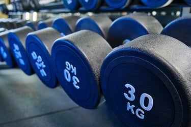 A row of heavy 30 kg black rubber dumbbells on a rack in a modern gym for strength training.