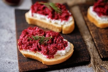 Beetroot and goat cheese crostini appetizer garnished with fresh dill on a rustic wooden board.