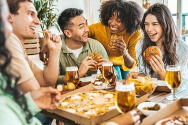 A diverse group of happy friends eating pizza and burgers with craft beer at a restaurant table.