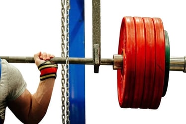 A powerlifter with wrist wraps grips a barbell loaded with heavy red weight plates in a gym squat rack.