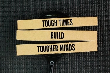 Inspirational quote on strips of paper reading tough times build tougher minds over a magnifying glass.