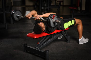A man performing a lying triceps extension skull crusher exercise using an EZ curl bar on a weight bench.