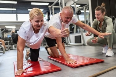 An active senior couple performing core exercises on mats with a personal trainer at the gym.