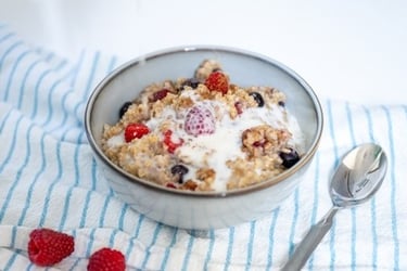 A bowl of healthy oatmeal porridge topped with fresh raspberries, blueberries, and a drizzle of milk.