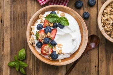 A wooden bowl of Greek yogurt topped with fresh blueberries, strawberries, and crunchy granola.