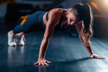 A fit woman in black sportswear performing a high plank exercise on a gym floor for core strength.