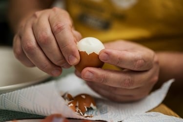 A person peeling a hard-boiled brown egg over a paper towel in a kitchen.