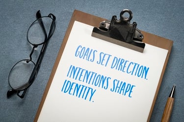 Motivational quote about goals and intentions on a clipboard with glasses and a pen.