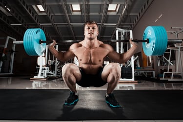A muscular man performing a heavy barbell back squat in a gym with blue weight plates.