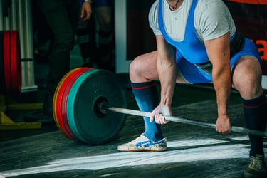 A powerlifter in a blue singlet performs a sumo deadlift with a heavily loaded barbell in a gym.